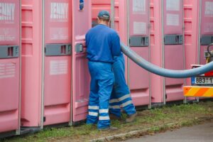 Two men dressed in blue work unifroms servicie a porta john.